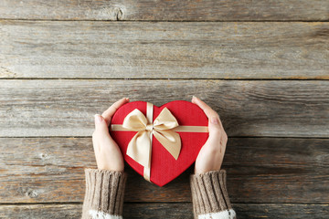 Female hands holding gift box on grey wooden background
