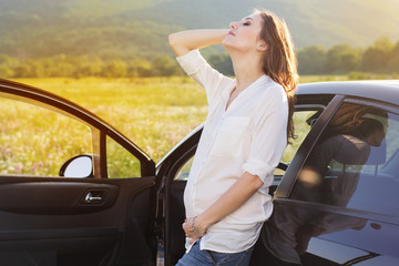 Pregnant happy young woman near car on the nature