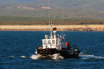 a small tugboat sails on the sea against the shore