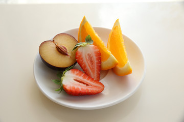 Half plum, strawberries and slices of oranges in white plate