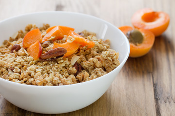 granola with fruits and nuts in white bowl on brown wooden background