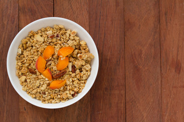 granola with apricot and nuts in white bowl on brown wooden background