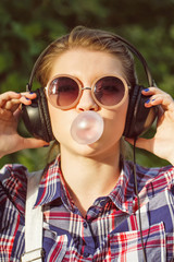 Hipster girl listening to music on headphones and chews the cud.