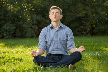 Naklejka na ściany i meble Teenager boy meditating and relaxing in a park
