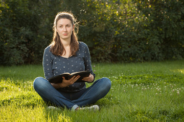 Teen girl reading the Bible outdoors at sunset time