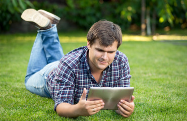 smiling student using digital tablet on grass at park