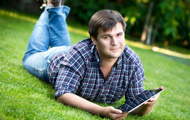 smiling man lying on grass at park and using digital tablet