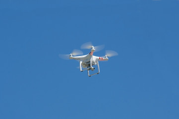 white drone hovering in a bright blue sky