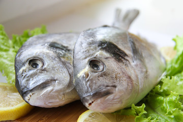 Fresh dorado on chopping board with lemon and vegetables