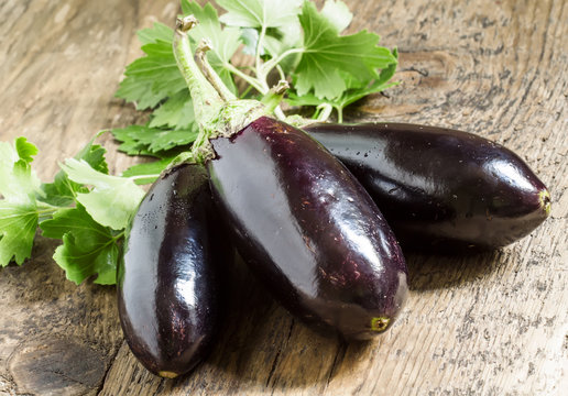 Small eggplant with tops on old wooden table, selective focus