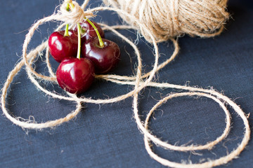 ripe cherries with a rough rope on a black background