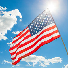 American flag waving in blue sky with sun behind it - close up