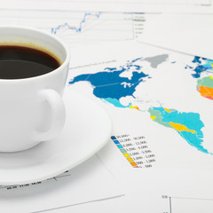 Coffee cup over world map and some financial documents - close up