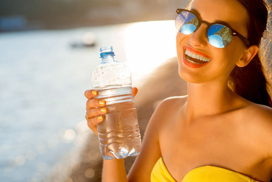Woman drinking water from transparent bottle on the beach