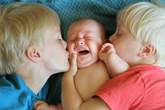 Young Brothers Kissing their Crying Newborn Baby Sister