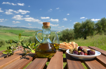 Olive oil, olives and bread on the wooden table against Tuscan l