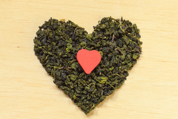 Green tea leaves heart shaped on wooden surface