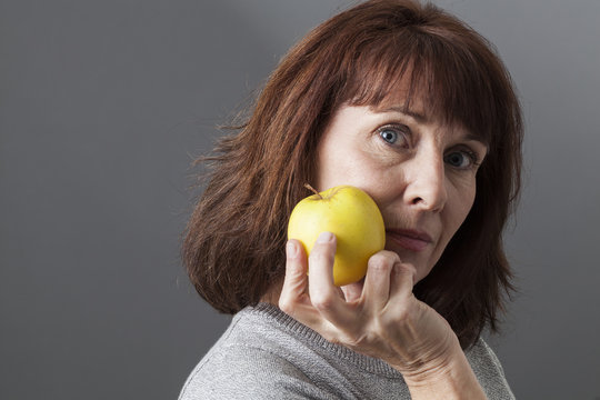 Thinking Beautiful Mature Woman Holding A Yellow Golden Apple For Vitamins Diet