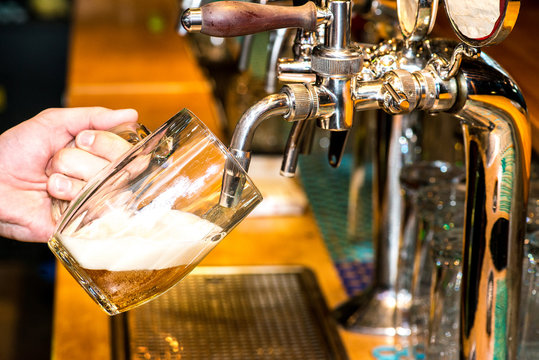 Close-up of bartender hand at beer tap pouring a draught lager beer