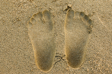 Two human footprints in the sand with a good shape and reflect the weight of a foot.