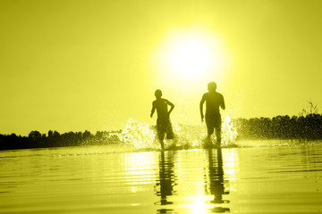 Glückliche junge Menschen laufen und springen am See beim Sonnenuntergang