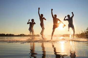 Fototapeta Glückliche junge Menschen laufen und springen am See beim Sonnenuntergang obraz