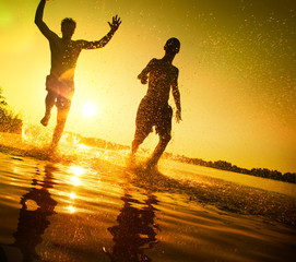Glückliche junge Menschen laufen und springen am See beim Sonnenuntergang