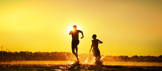 Glückliche junge Menschen laufen und springen am See beim Sonnenuntergang