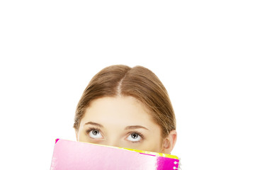 Teen woman hiding behind a notebook.