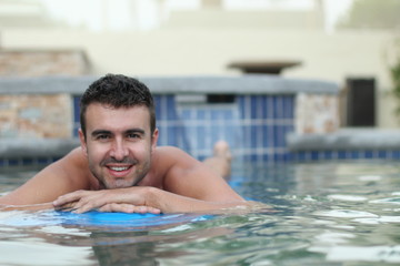 Sexy young man floating on a mattress in water pool

