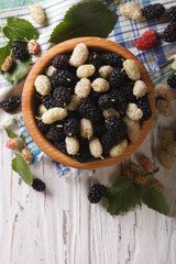 White and black mulberries in a wooden bowl vertical top view
