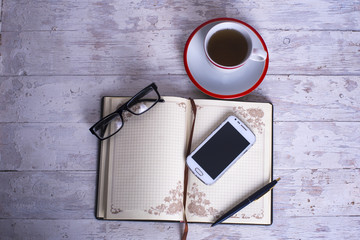 Naklejka premium cup, notepad, cellphone, glasses and pen on white vintage wooden background