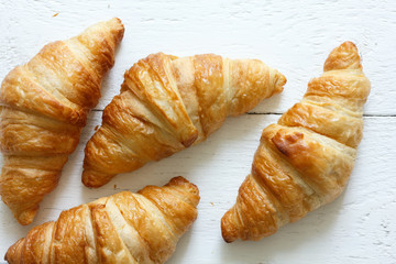 Golden croissants on rustic white wood, from above.