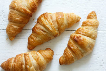 Golden croissants on rustic white wood, from above.