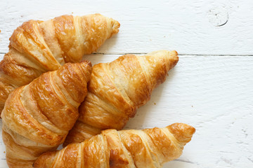 Golden croissants on rustic white wood, from above.