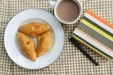 Coffee cup with a croissant on brown fabric