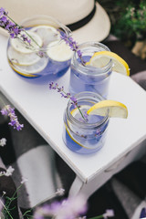 Homemade lavender lemonade with fresh lemons on a white wooden tray in a lavender field