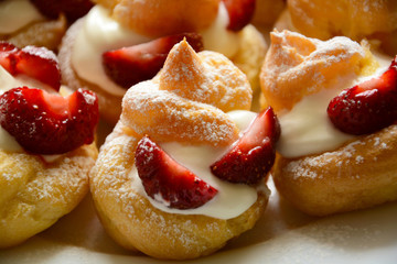 Homemade eclairs with strawberries on dark wooden background