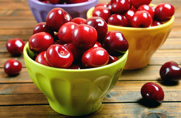 Colorful bowl with cherries on wooden table