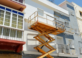 Plataforma elevadora de tijera para el arreglo de la fachada de una casa - obrazy, fototapety, plakaty