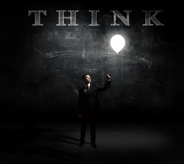 Obraz premium Young man holding a light at his hands against dark background with a word think