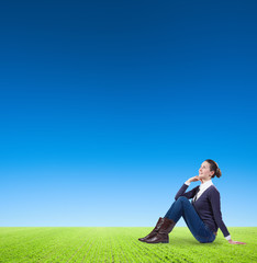 A business woman looking up and sitting on green grass with blue clean sky