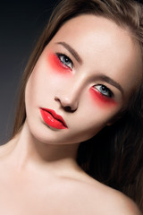 Beautiful girl with bright creative makeup. Red lips, perfect skin. Portrait shot in the studio on a black background.