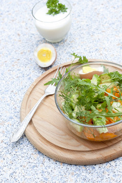 Salad with fresh vegetables and herbs in a glass bowl on a wooden board, boiled eggs and yogurt with herbs