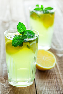 Two glasses of drink with lemon and fresh mint on wooden table.