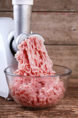 Mincer machine with fresh chopped pork meat on wooden background