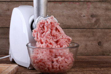 Mincer machine with fresh chopped pork meat on wooden background