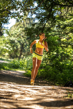Woman running in wooded forest area, training and exercising on beautiful summer day