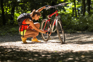 Pausing her mountain bike ride, female takes a break, admiring the natural beauty surrounding her in the forest. She's repairing her bike.	
