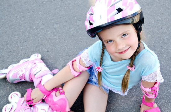 Cute smiling little girl in pink roller skates and protective ge